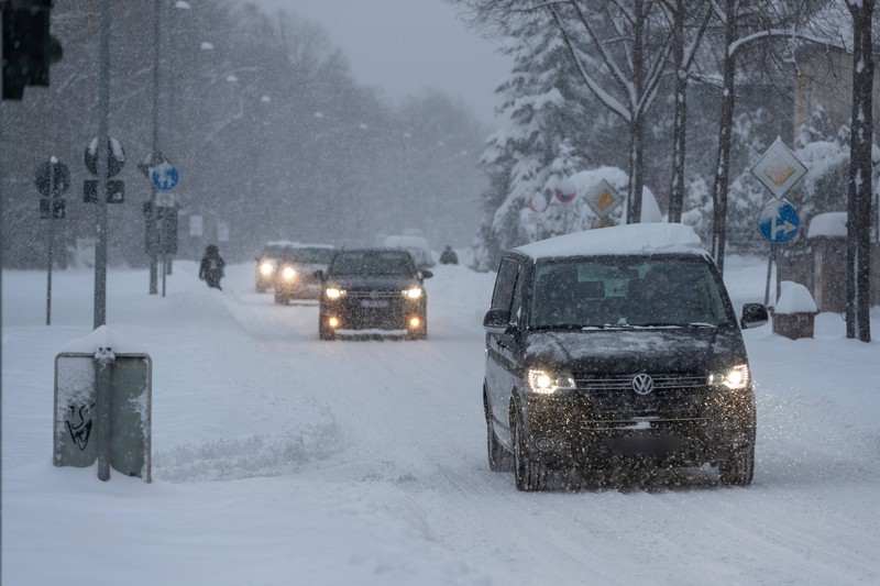 Autos fahren mit eingeschaltetem Abblendlicht über eine schneebedeckte Straße.