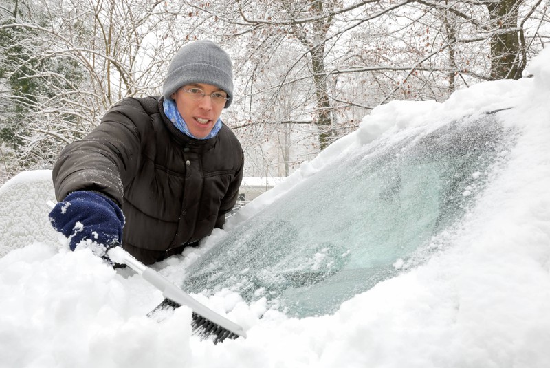 Ein Mann befreit die Frontscheibe seines Autos vom Schnee.