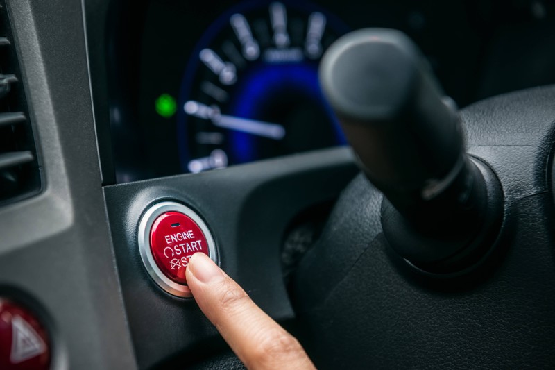 Zu sehen ist eine Hand, die den Start/Stop-Knopf in einem Auto drückt.
