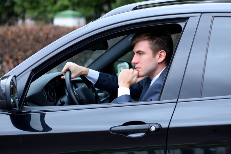 Zu sehen ist ein junger Mann, der am Steuer eines Autos sitzt.