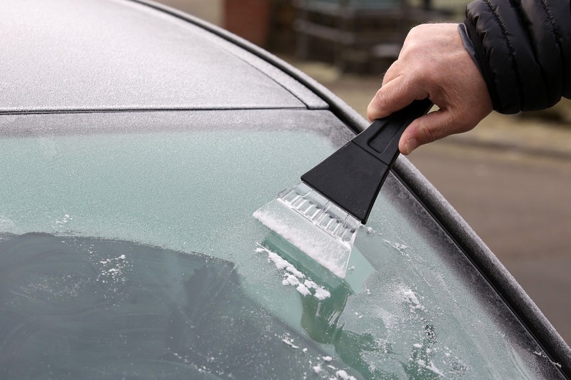 Ein Autofahrer kratzt im Winter das Eis von seiner Scheibe