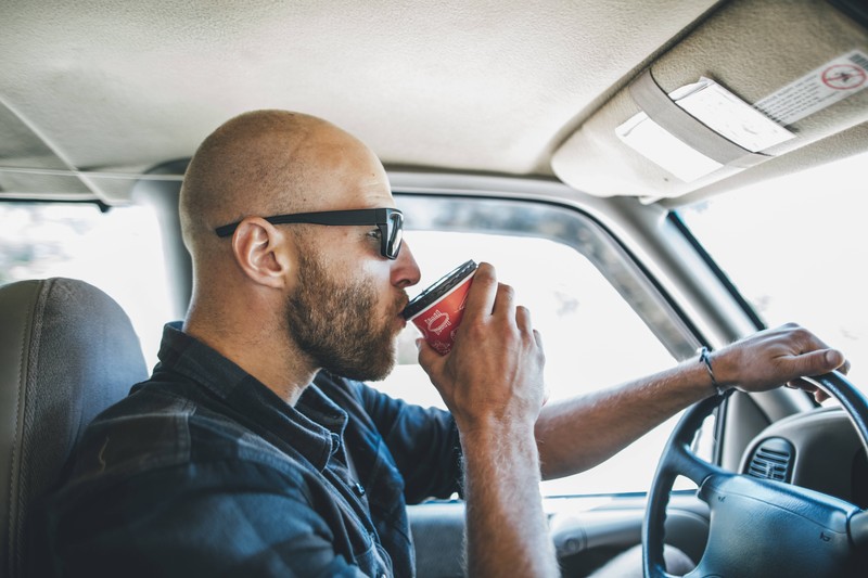 Das Bild illustriert einen Mann, der im Auto etwas trinkt, was bei Hitze wichtig ist