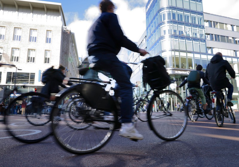 Zu sehen sind Fahrradfahrer, die in der Innenstadt über einen Platz fahren.